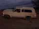 1988 Ford Bronco - A tan Jeep Cherokee Chief is driven off-road under a cloudy sky.