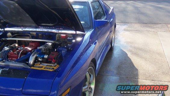 Blue sports car engine bay with exposed engine components and hood open