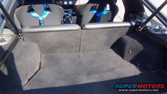 Interior view of racing seats with blue harnesses and carpeted cargo area