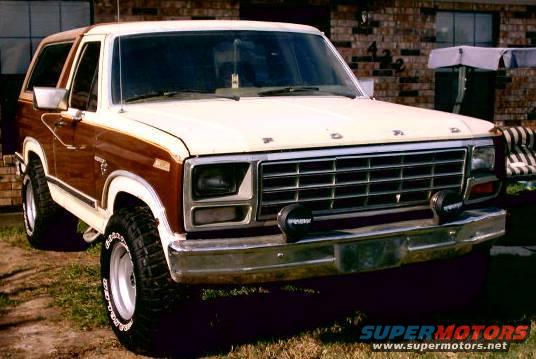 White and wood-paneled 1980 Ford Bronco with aftermarket wheels and fog lights