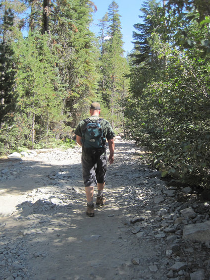 Guy with a backpack walks down a rocky, wooded trail