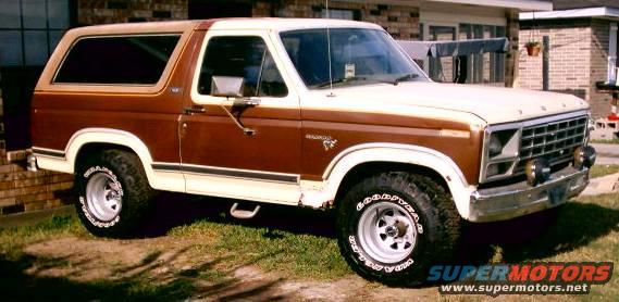 Brown and white Ford Bronco with aftermarket wheels parked on grass