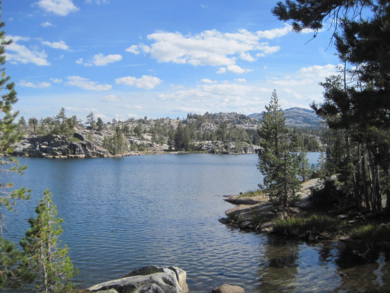 Lake with rocky shores and pine trees under a blue sky with clouds