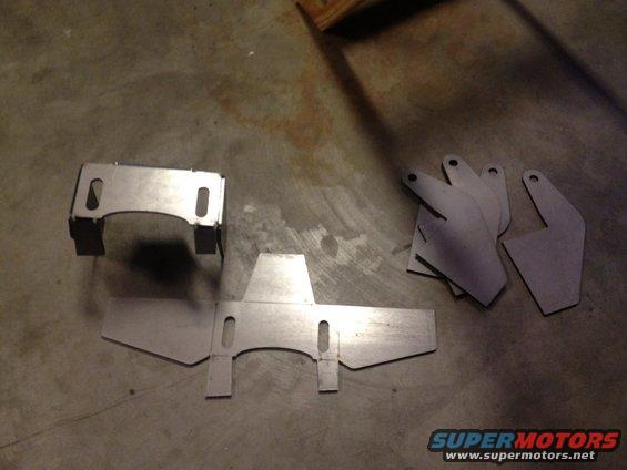 Metal brackets and flat pieces laid out on a concrete floor