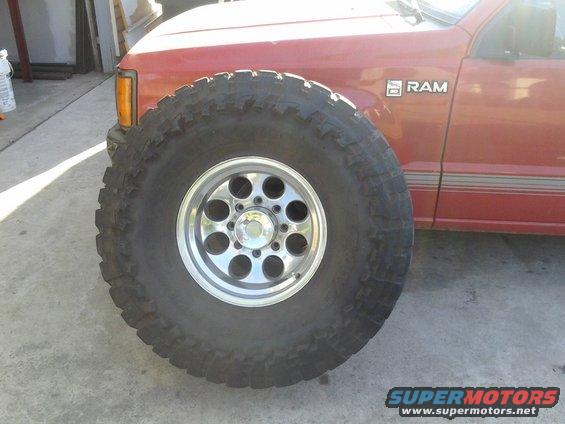 Red truck side with a large off-road tire and chrome rim in the foreground