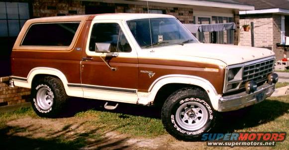 Brown and white Ford Bronco with aftermarket wheels parked on grass