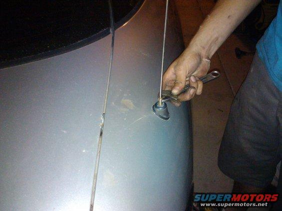 Hand using a wrench to tighten a car antenna base on a silver vehicle's fender