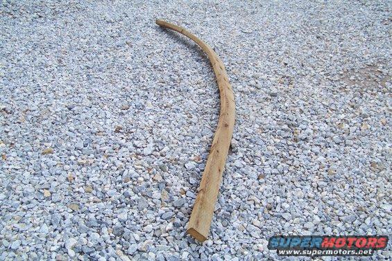 Curved wooden stick lying on a bed of grey gravel. Watermark reads SUPER MOTORS