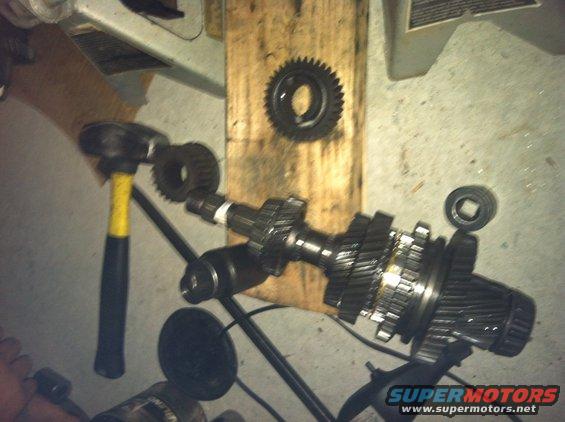 Transmission gears laid out on a wooden board with a hammer nearby