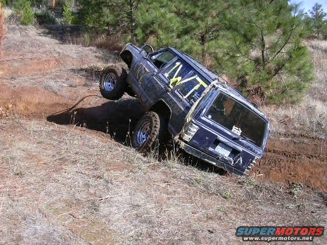 Dark blue SUV with yellow roll cage tilted on an off-road trail