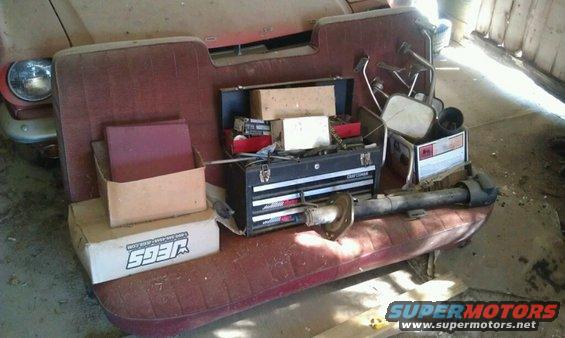 Car interior with red bench seat, toolbox, boxes, and driveshaft