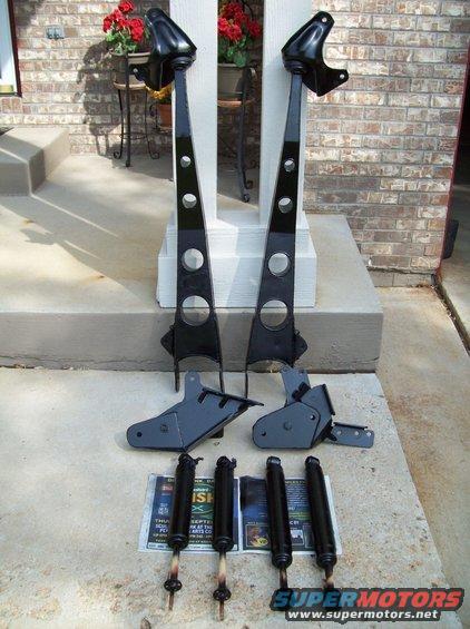 Four shock absorbers and two black suspension lift brackets on concrete