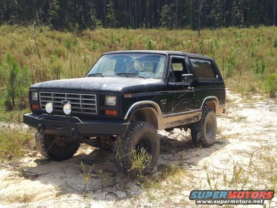 Black 1986 Ford Bronco with aftermarket bumper and off-road tires parked on sandy terrain