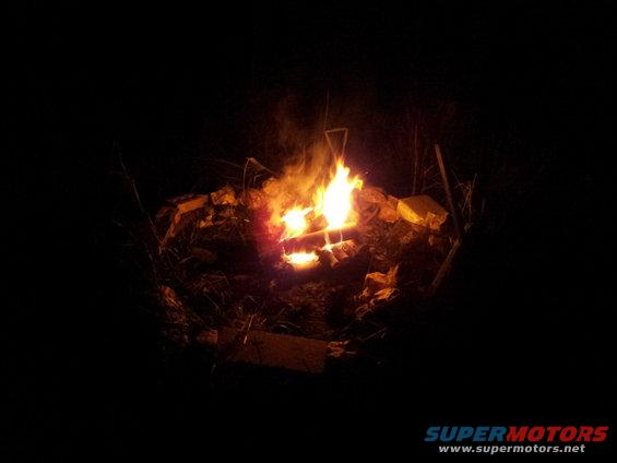 Campfire burning at night, surrounded by rocks and dry grass