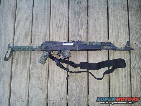 Assault rifle with camouflage pattern and sling on wooden deck