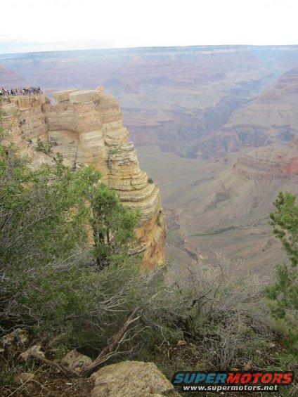 Grand Canyon vista with a cliff edge and tourists, foreground brush
