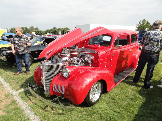 Red 1939 sedan with hood open, chrome grille, custom engine, and chrome bumper. Two people stand nearby