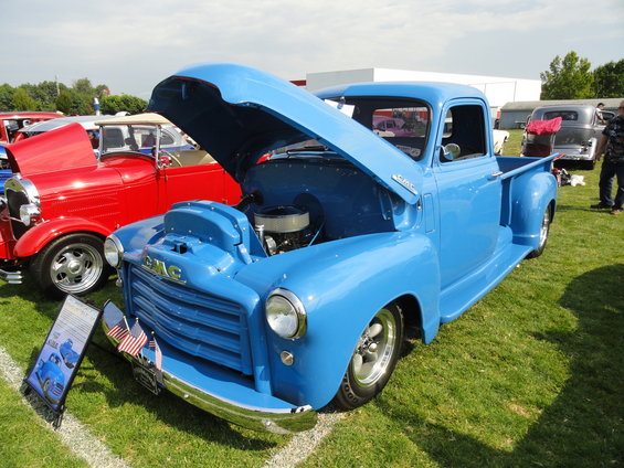 Blue 1950s GMC pickup truck with hood open, chrome grille, and custom wheels parked on grass