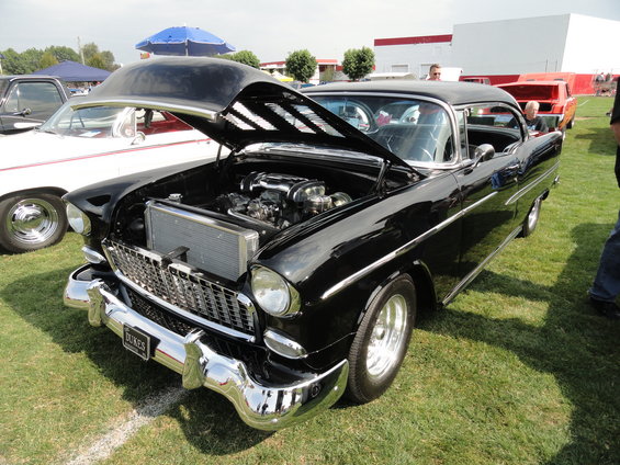 Black 1955 Chevrolet Bel Air with hood open, showing engine and chrome grille. "DUKES" plate visible