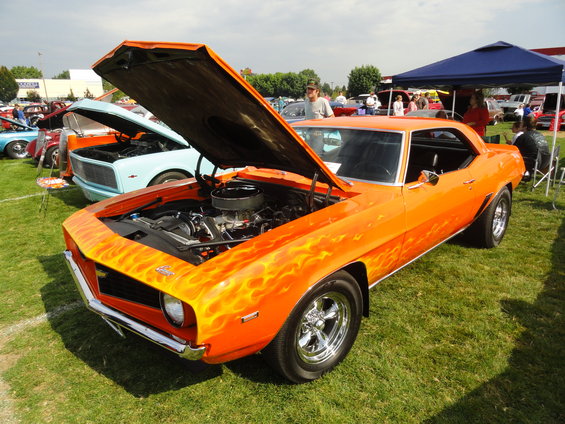 Orange 1969 Chevrolet Camaro with flame decals and hood open, parked on grass at a car show