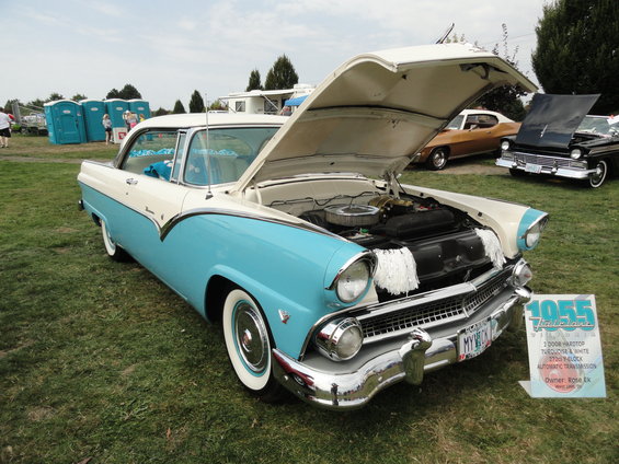 Two-tone turquoise and white 1955 Ford Fairlane with hood open, parked on grass