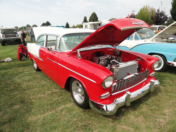 Red and white 1955 Chevrolet with hood open, parked on grass