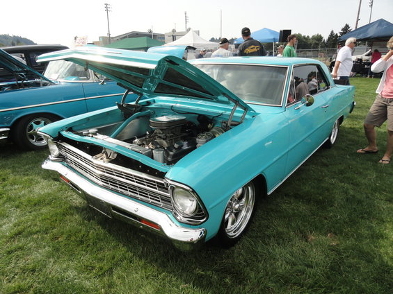 Turquoise 1966 Chevrolet Nova II coupe with hood open, parked on grass next to another classic car