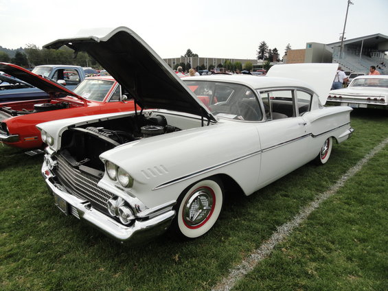 White 1958 Chevrolet Bel Air with hood open, parked on grass at a car show