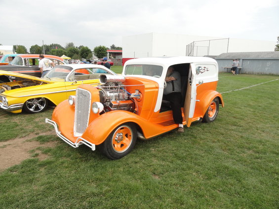 Orange and white panel van hot rod with exposed engine, person getting out. Yellow car in background