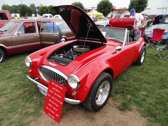 Red 1963 Austin Healey 3000 Mark III convertible with hood open, parked on grass next to a wood-paneled station wagon