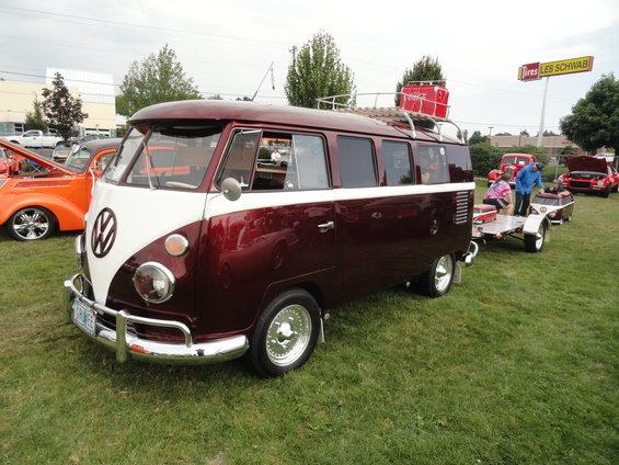Maroon and white Volkswagen Type 2 van with a roof rack and a red cooler, parked on grass