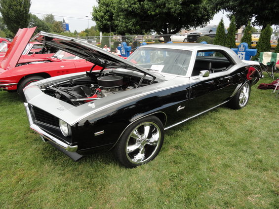 Black and silver 1969 Chevrolet Camaro coupe with hood open, chrome wheels, parked on grass