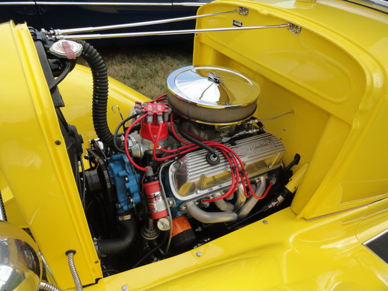 Yellow car engine bay with chrome air cleaner, red spark plug wires, and silver valve covers