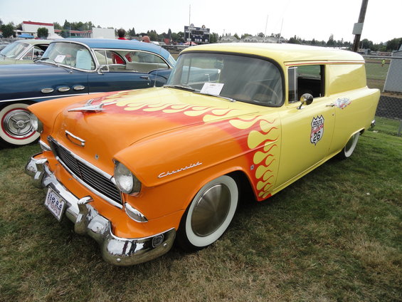 1955 Chevrolet Nomad panel van with orange and red flames on hood and side, Route 66 emblem on door. Another car is parked to the left