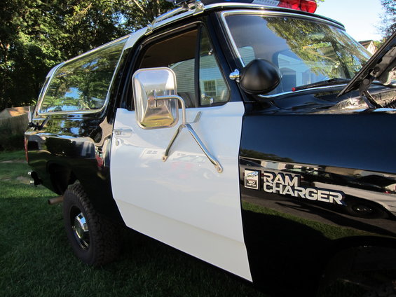 Side view of a black and white Dodge Ramcharger with 'RAM CHARGER' badging. Police light bar on roof