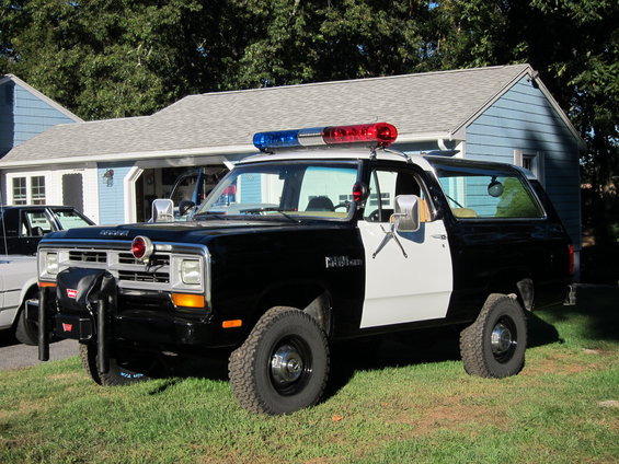 Black and white police SUV with light bar, parked on grass in front of a house