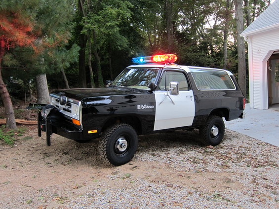 1987 Dodge Ramcharger police SUV with light bar and push bumper, parked on gravel