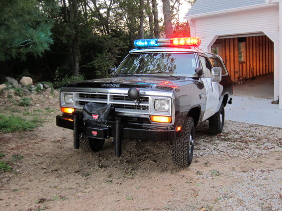 Black and white police SUV with light bar, parked in front of a garage