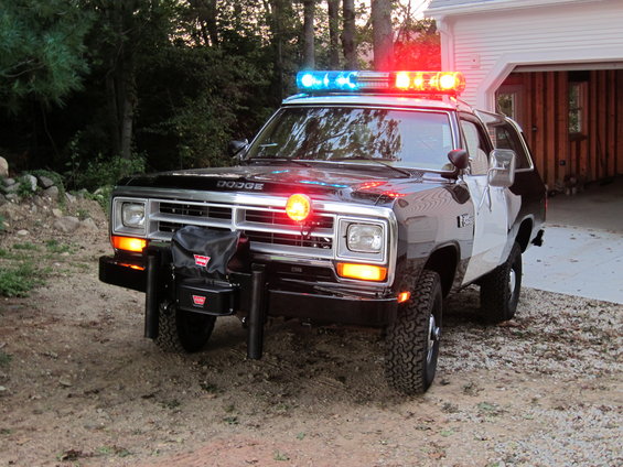 Front view of black and white police SUV with light bar and winch. Dodge badging visible