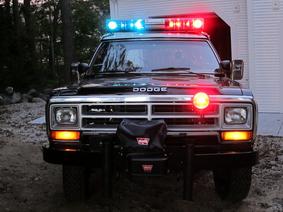 Front view of a black Dodge Ram truck with a light bar and siren, equipped with a Warn winch