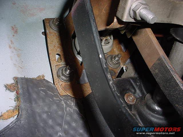 Close-up of rusty metal bracket and black plastic pedal assembly with visible bolts and frayed material