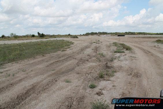 Dirt road with tire tracks in a dry, grassy landscape under a cloudy sky