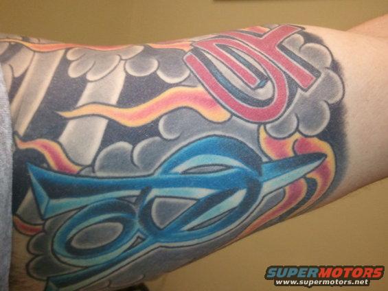 Tattoo on arm with blue and red lettering and abstract shapes