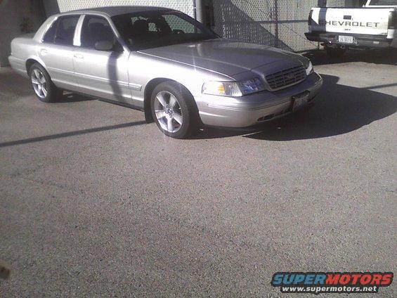 Silver 2003 Ford Crown Victoria sedan parked on asphalt, front quarter view. Some damage visible on the front bumper