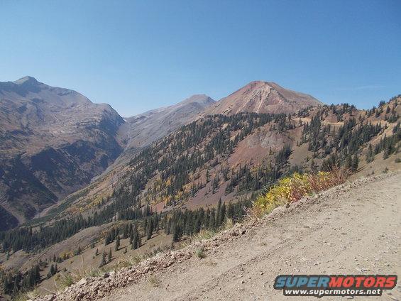 mountain valley with trees and a dirt road in the foreground, clear blue sky above