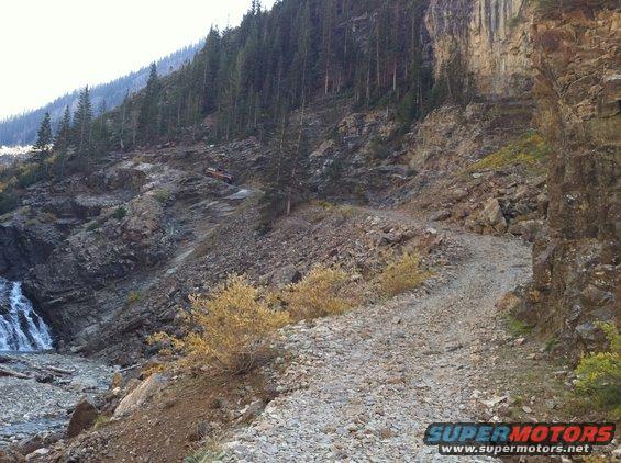 Orange SUV on a rocky mountain road with a waterfall