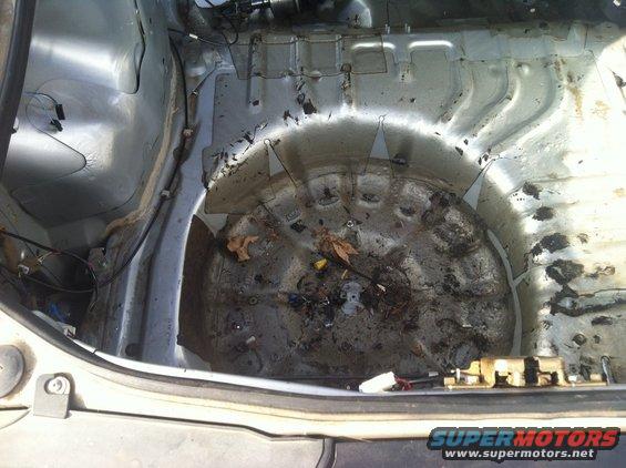 Inside of a dirty car trunk, showing the spare tire well and surrounding metal