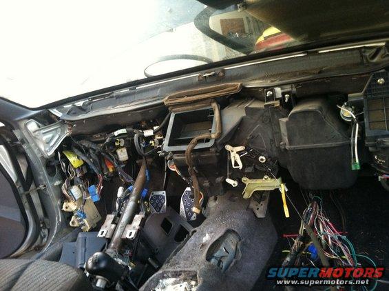 Car interior with dashboard removed, showing wiring harness and HVAC components