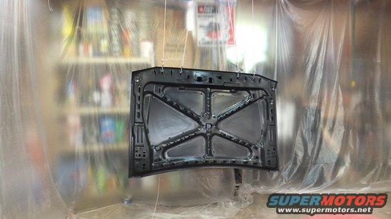 underside of a car hood hanging, being prepped for paint