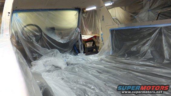 Vehicle interior covered in plastic sheeting, likely for painting. Steering wheel visible